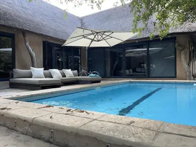 a swimming pool with an umbrella next to a house at Simba Safaris African Pride Exotic Lodge in Lephalale