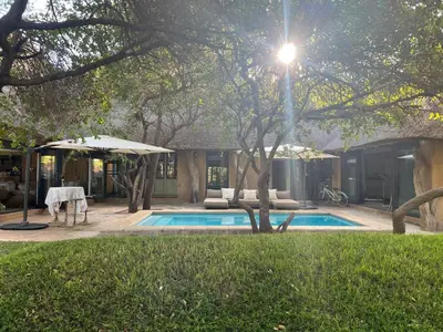 a swimming pool with an umbrella next to a house at Simba Safaris African Pride Exotic Lodge in Lephalale