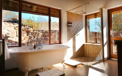 a bath tub in a bathroom with a stone wall at Shibula Safari Lodge in Welgevonden Game Reserve