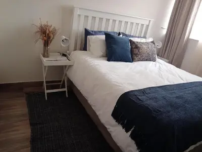 a bed with blue pillows and a night stand with a table at Private Room Chez Khanyi Homestays in Pretoria