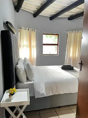 a bedroom with a bed with white sheets and a window at Indlovu Inn Guesthouse in Graskop