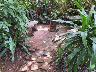 a brick pathway with a bench and a table in a garden at The Crooked Forest in Pretoria