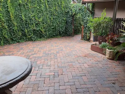 a brick patio with a table in front of a hedge at The Crooked Forest in Pretoria