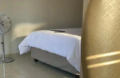 a bedroom with a bed with white sheets and a fan at Yami Nawe Lodge in Dennilton