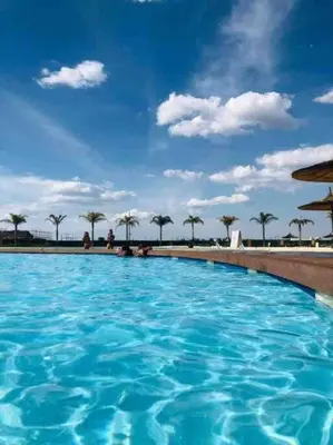 a large blue swimming pool with palm trees in the background at THE BLYDE LAGOON BEACH PRETORIA 3 BEDROOM GROUND FLOOR APARTMENT in Pretoria