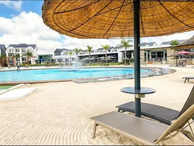 a chair with an umbrella next to a swimming pool at THE BLYDE LAGOON BEACH PRETORIA 3 BEDROOM GROUND FLOOR APARTMENT in Pretoria
