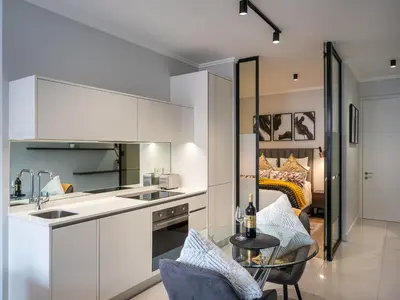a kitchen with white cabinets and a table and a bed at eKhaya at Ellipse Waterfall City in Midrand