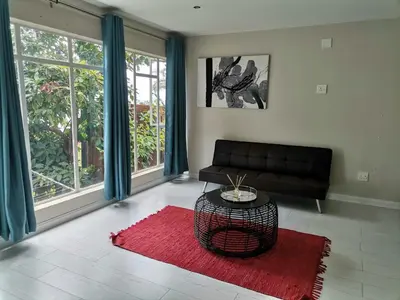 a living room with a black couch and a red rug at Manz' amahle Guest Cottage in Hartbeespoort