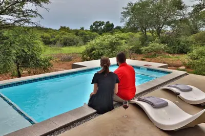 a man and woman sitting next to a swimming pool at Umkhaya in Marloth Park