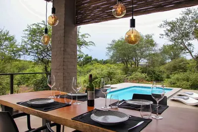a dining table with wine glasses and a pool at Umkhaya in Marloth Park