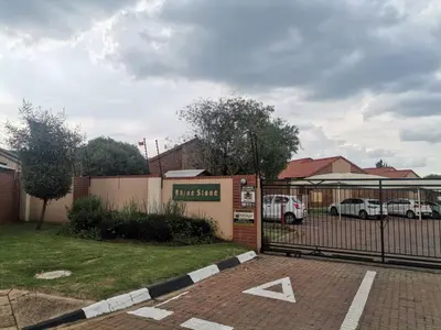 a gate to a parking lot with two cars parked at Centurion Cosy Apartment in Centurion