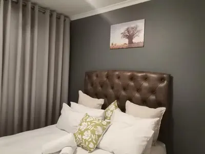 a bedroom with a bed with white pillows and a tree at Centurion Cosy Apartment in Centurion