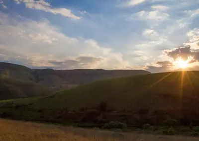 a sunset over a green field with the sun shining on it at Highland Run Fly Fishing Estate by Dream Resorts in Lydenburg