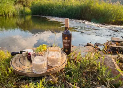a bottle of wine and glasses on a table next to a river at Highland Run Fly Fishing Estate by Dream Resorts in Lydenburg