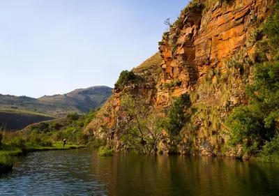 a river in front of a rocky mountain with trees at Highland Run Fly Fishing Estate by Dream Resorts in Lydenburg