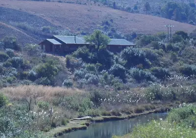 a house on the side of a hill next to a river at Highland Run Fly Fishing Estate by Dream Resorts in Lydenburg