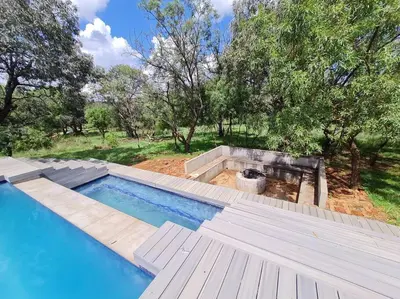 an empty swimming pool with a wooden deck and trees at No 16 Elements - 5 Bedroom Beauty in Moheme