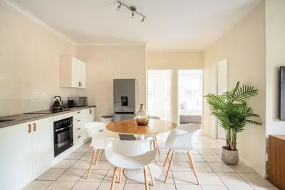 a kitchen with a wooden table and white chairs at Beautiful Two Bedroom Appartment In Hatfield in Pretoria