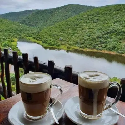 two cups of coffee sitting on a table overlooking a river at Livingstone Bush Lodge, Mabalingwe in Bela-Bela