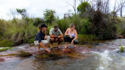 three people sitting on a rock in a stream at Nungubane Game Lodge in Welgevonden Game Reserve