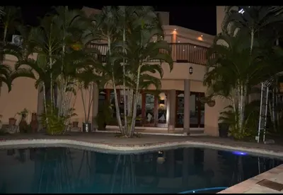a swimming pool in front of a building with palm trees at Tengo guest house in Phalaborwa
