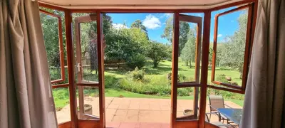 an open window with a view of a garden at DullVino Cottage no 15 at Critchley in Dullstroom