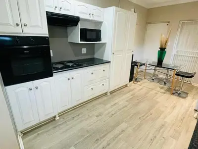 a kitchen with white cabinets and a wooden floor at Grace Gardens - Grace in Pretoria