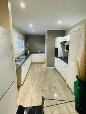 a kitchen with white cabinets and a wooden floor at Grace Gardens - Grace in Pretoria