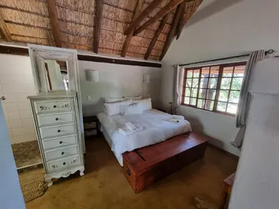 a bedroom with a bed and a dresser and windows at Milkwood Cottage Mabalingwe in Bela-Bela