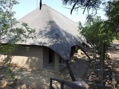 a small building with a thatched roof with trees at Balule Bushveld Safari Lodge in Phalaborwa