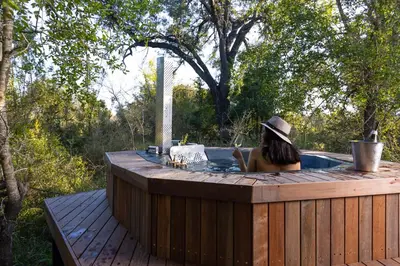 a woman sitting in a hot tub on a wooden deck at Simbavati Waterside in Klaserie Private Nature Reserve