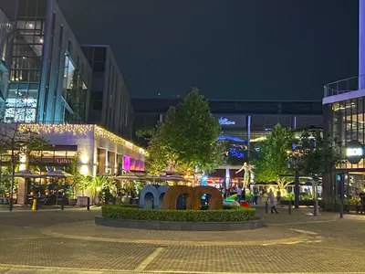 a city square at night with a tree and buildings at Menlyn Maine Residences - Kyoto king size xl bed in Pretoria