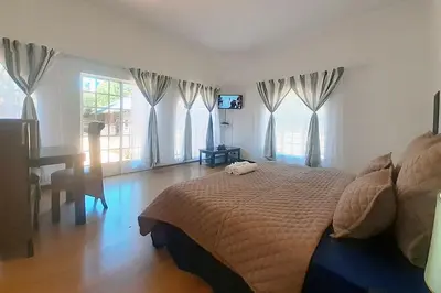 a bedroom with a bed and a desk and windows at Queens Palace in Pretoria