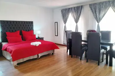 a bedroom with a red bed with a desk and chairs at Queens Palace in Pretoria