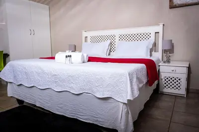 a white bed with a red blanket and white pillows at Lempitse Lodge in Moletlane