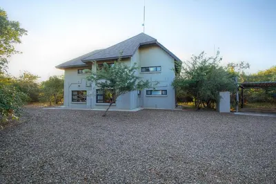a white house with a tree in front of it at Call of the Fish Eagle Self-catering Holiday Home with solar in Marloth Park