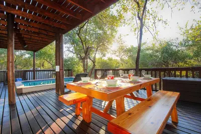 a wooden deck with a table and benches on it at Call of the Fish Eagle Self-catering Holiday Home with solar in Marloth Park