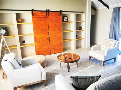 a living room with white furniture and a wooden cabinet at Ostrich Hide in Marloth Park