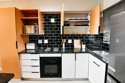 a kitchen with white cabinets and a black tile wall at Unit 508 at Menlyn Place in Pretoria
