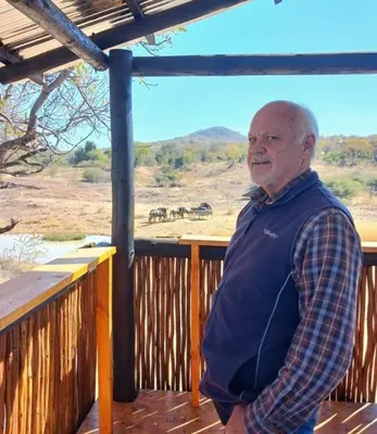 a man standing on a deck with an elephant in the distance at Ebenhaeser overnight accomodation in Bela-Bela