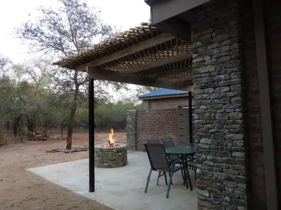 a patio with a table and chairs under a wooden pergola at Locust Retreat in Marloth Park in Marloth Park