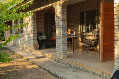 a woman sitting on a patio on a house at Mackers Self Catering Cottages in Hazyview