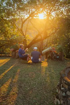 two men sitting on the grass under a tree at Mackers Self Catering Cottages in Hazyview