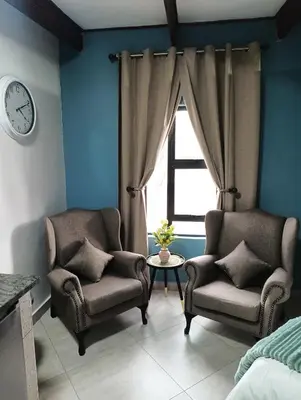 two chairs and a table in a room with a clock at Unique Overnight Polokwane in Polokwane