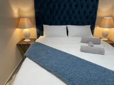 a large bed with a blue headboard and two lamps at Mall of Africa Spot By Damo in Midrand