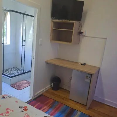 a room with a television and a table with a refrigerator at Moonlight Guesthouse in Pretoria