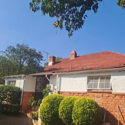 a brick house with a red roof and bushes at Moonlight Guesthouse in Pretoria