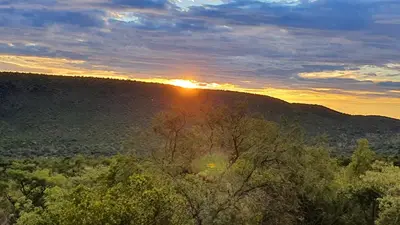 a sunset over a hill with trees in the foreground at 113 Zwartkloof Private Game Reserve Bela-Bela in Bela-Bela
