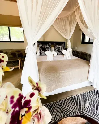 a bedroom with a bed with curtains and flowers at Baluleni Safari Lodge in Grietjie Nature Reserve