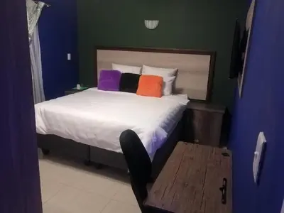 a bedroom with a bed with colorful pillows and a chair at Munach Guest Lodge in Benoni